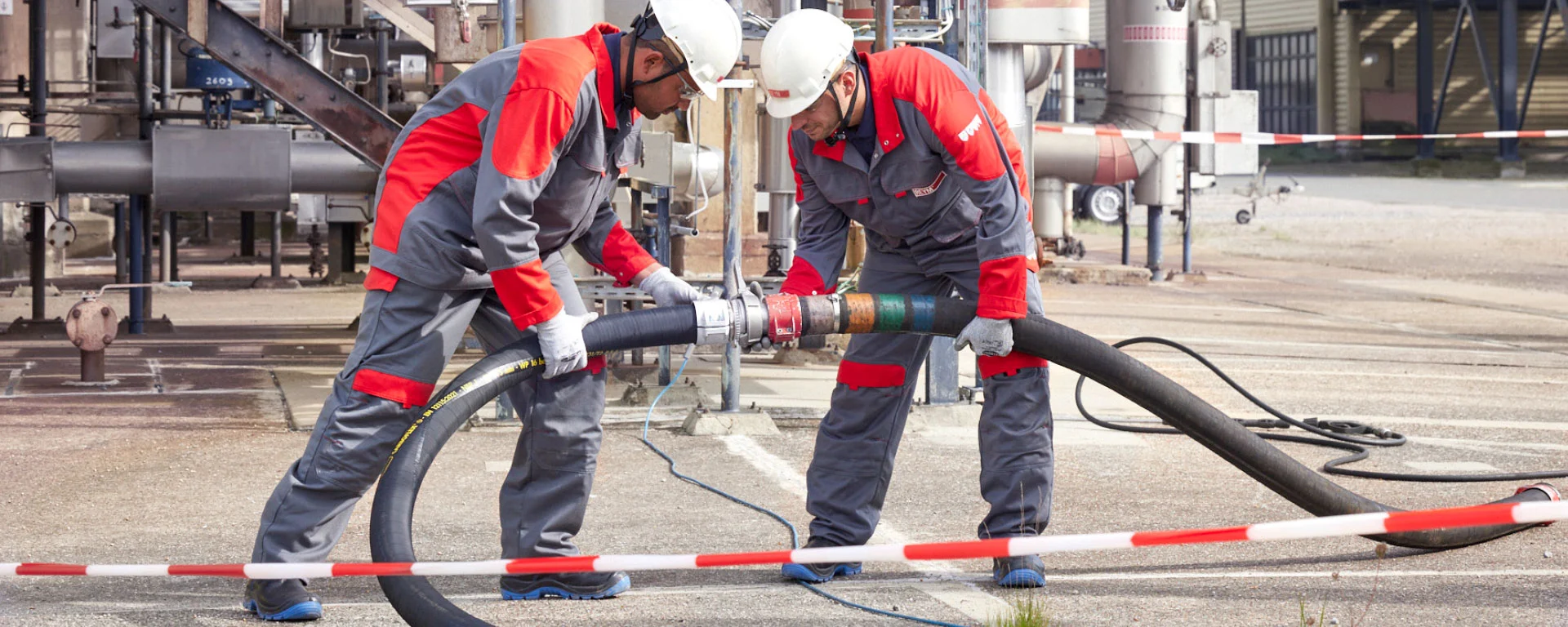 Zwei REYM-Mitarbeiter in persönlicher Schutzausrüstung (PSA) verbinden einen Schlauch vor einer Industrieanlage