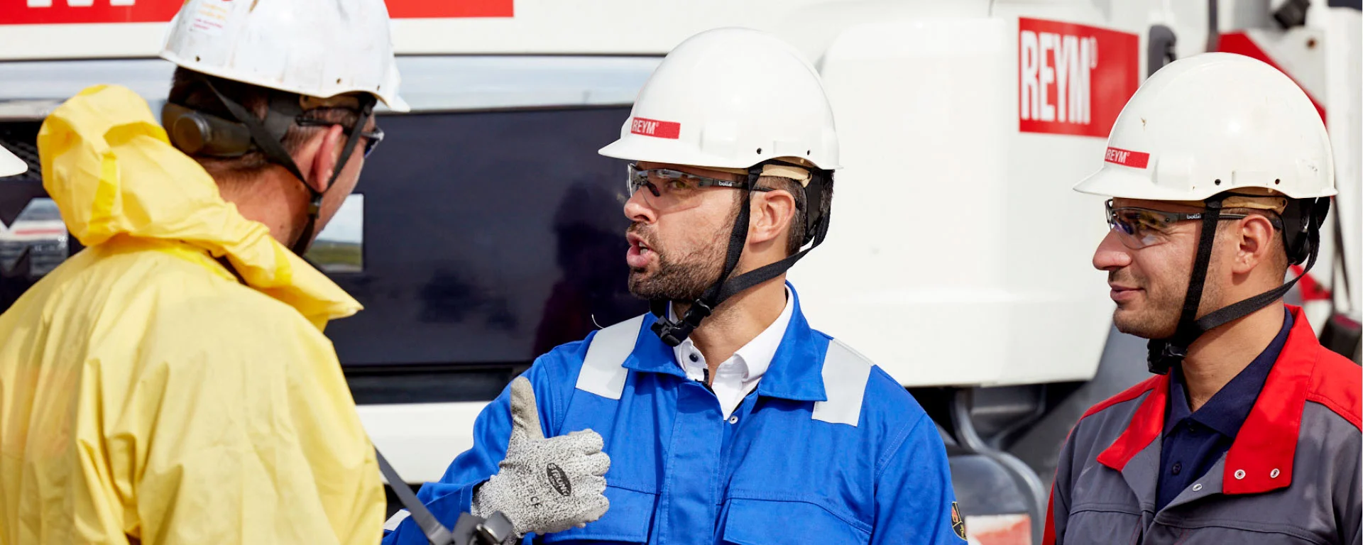 Drei REYM-Kollegen in verschiedener PSA mit Helmen im Gespräch – ein Kollege zeigt Daumen hoch