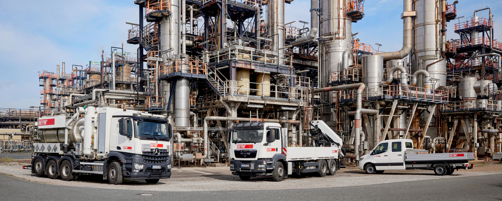 Drei REYM-Fahrzeuge, darunter ein LKW und eine Pritsche, vor einer Industriekulisse