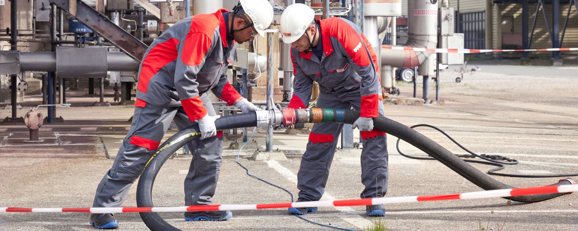 Zwei REYM-Mitarbeiter in persönlicher Schutzausrüstung (PSA) verbinden einen Schlauch vor einer Industrieanlage